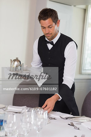 Waiter holding tray and setting table