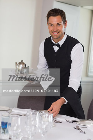 Happy waiter holding tray and setting table