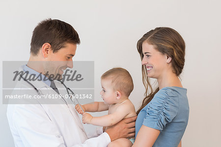 Handsome pediatrician checking baby boy held by his mother
