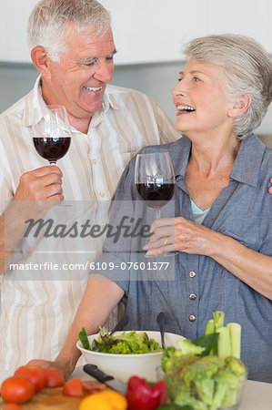 Smiling senior couple preparing a salad and having red wine
