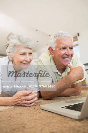 Cheerful senior couple using the laptop together lying on rug