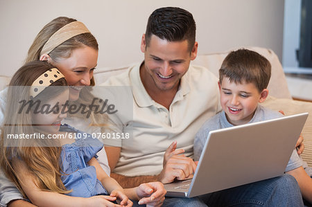 Happy family of four using laptop in living room