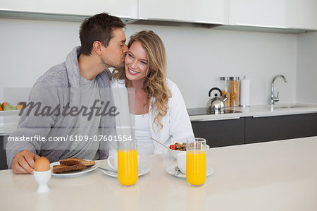 Man kissing happy woman at breakfast table
