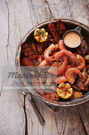 Shrimp Boil with grilled andouille sausage, fried potatoes, and remoulade sauce on wooden surface