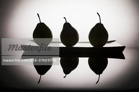 Black silhouettes of pears on a plate, and reflection