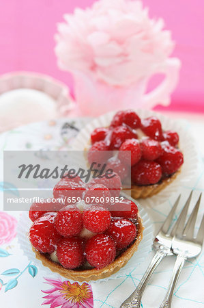 Two strawberry tartlets and cake forks on a floral tablecloth