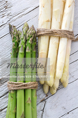 Green and white asparagus, tied in bundles, on a wooden surface