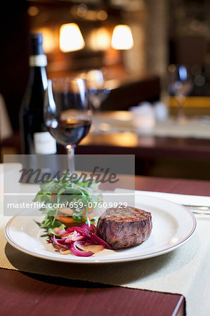 a view on the interior of the restaurant, a table with wine, a dish of sirloin steak with red onions, tomatoes and rocket leaves