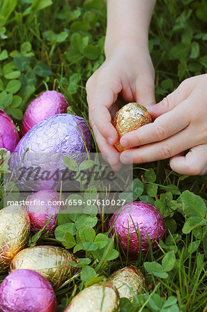 Child's hand reaching for a chocolate egg in a field