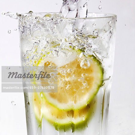 Water being poured into a glass of lime slices