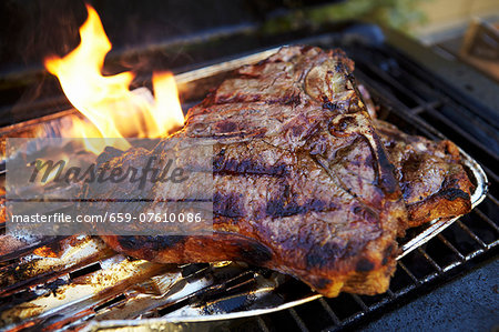 A T-bone steak in an aluminium tray on a barbecue