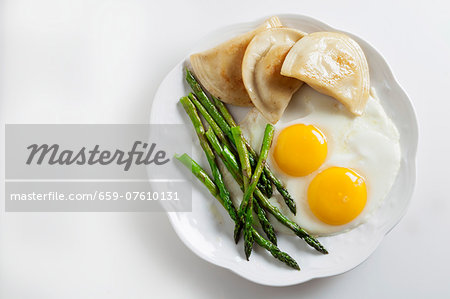 Two fried eggs with pierogi and green asparagus