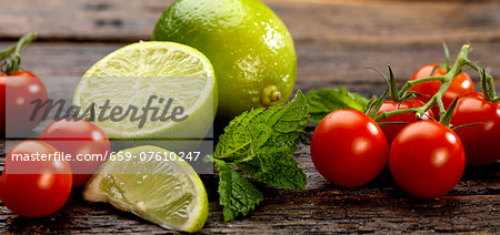 Cherry tomatoes, mint and limes on a wooden surface