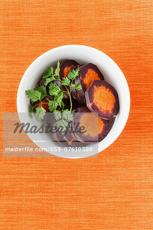 Slices of purple carrots in a white bowl with coriander leaves