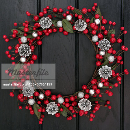 Christmas wreath with red and silver bauble decorations and pine cones over dark oak wood background.