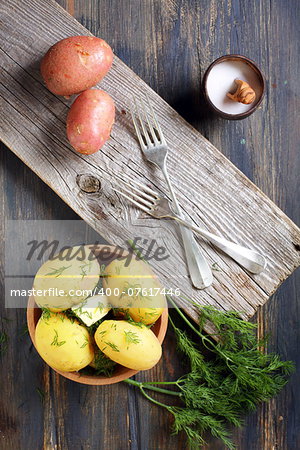 Boiled potatoes, dill and fork on old wooden table.