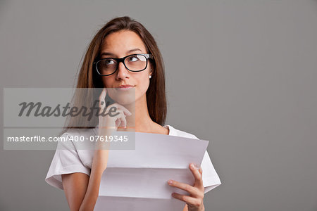 brunette girl with glasses thinking about news she received on a white document on a neutral gray faded background