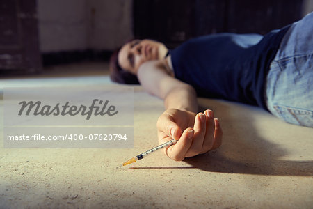 Closeup of young girl in heroine overdose holding syringe and lying on pavement. Copy space