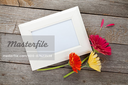 Three colorful gerbera flowers and photo frame on wooden table