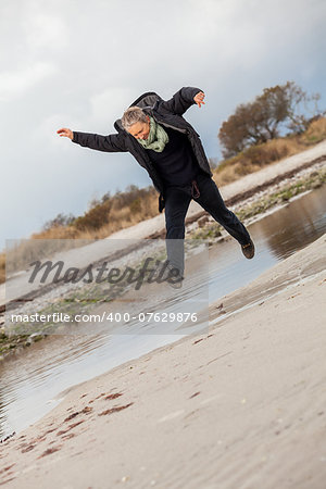 Happy senior woman frolicking on the beach striding along with outspread arms and a smile of appreciation as she enjoys nature and the freedom of her retirement