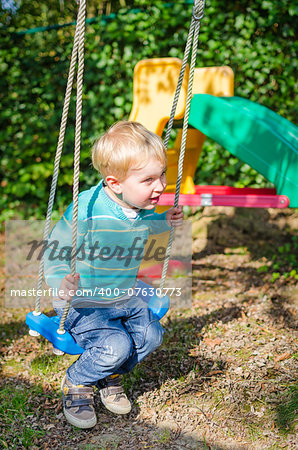 Cute little blond boy swinging on swings in the outdoor playground