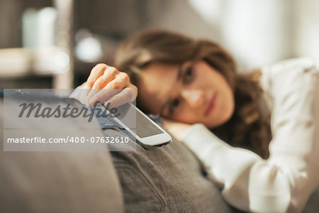 Closeup on thoughtful young woman with cell phone sitting on couch