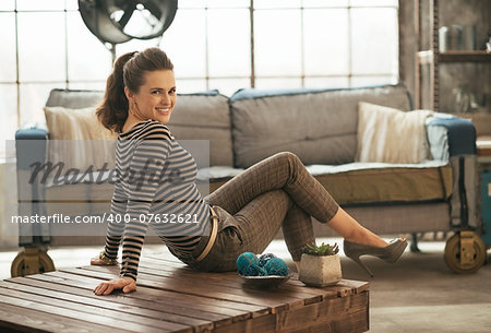 Happy young woman sitting on coffee table in loft apartment