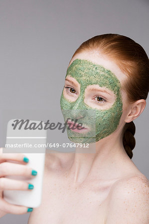 Young woman wearing face mask, taking self portrait photograph with smartphone