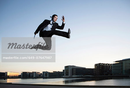 Mid adult businessman jumping mid air, Copenhagen harbor, Denmark