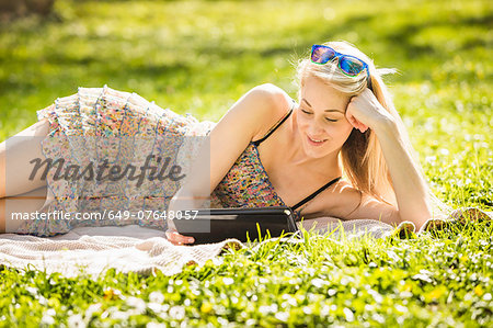 Young woman lying in forest looking at digital tablet