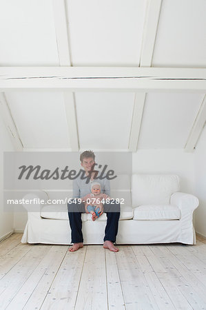 Portrait of mature father with baby daughter on sofa