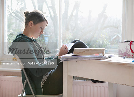 Sixteen year old girl studying and writing notes next to window