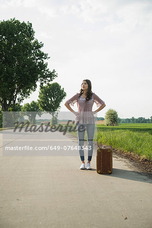 Young woman standing on country road with suitcase