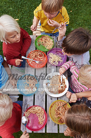 Overhead view of seven children eating spaghetti at picnic table