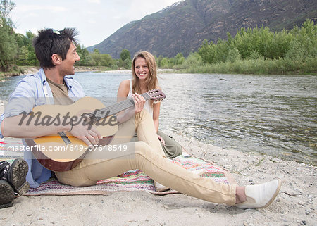 Friends sitting beside river, playing guitar