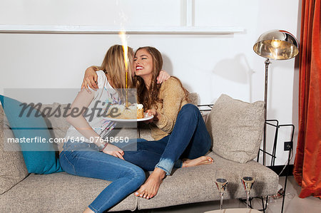 Young women with cake hugging on couch
