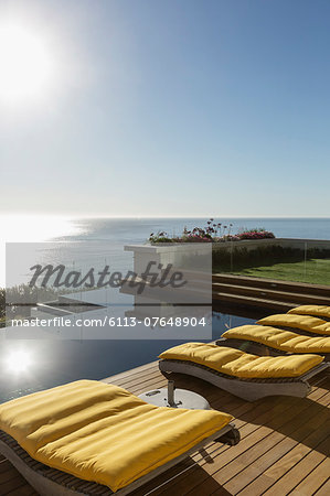 Sun shining over lounge chairs at poolside overlooking ocean