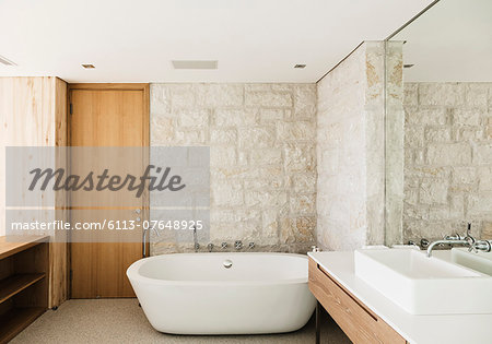 Stone walls behind soaking tub in modern bathroom