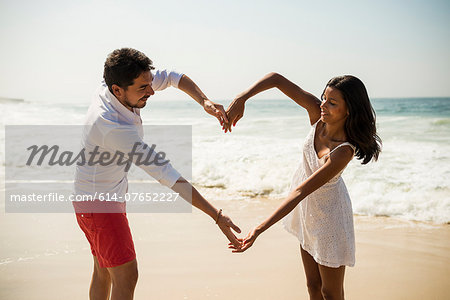 Couple making heart shape with arms on Arpoador beach, Rio De Janeiro, Brazil