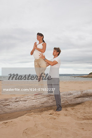 Pregnant mid adult woman with personal trainer practicing yoga at beach
