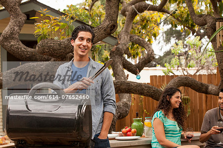 Man cooking on barbecue, friends in background