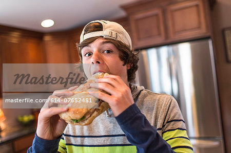 Teenage boy in kitchen biting large sandwich Teenage boy in kitchen biting large sandwich