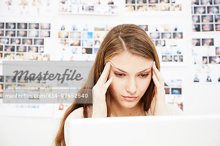 Young woman using computer rubbing head