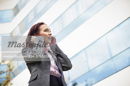 Young female businesswoman talking on smartphone outside office