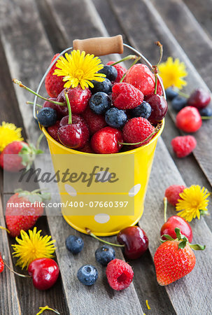 Fresh cherry, strawberry, blueberry and raspberry in a bucket on wooden table