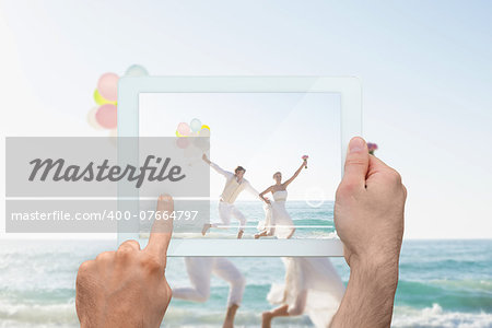 Hand holding tablet pc showing newlyweds having fun holding balloons