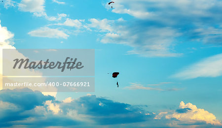 silhouettes of unidentified skydivers parachutist on blue sky on sunset
