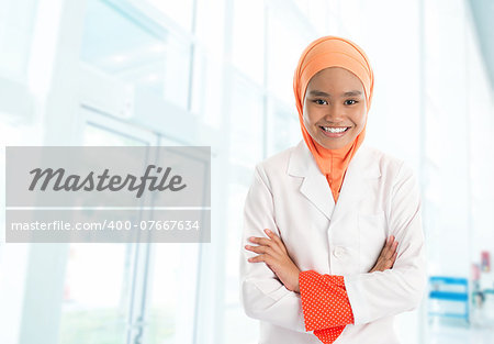 Cheerful young Muslim female nurse portrait, standing inside hospital