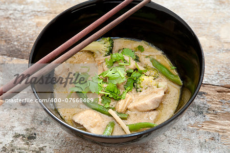 Bowl of delicious healthy creamy Thai green curry with diced chicken pieces served with chopsticks, high angle view