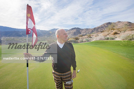 Senior male golfer looking away while holding flag and putter at golf course
